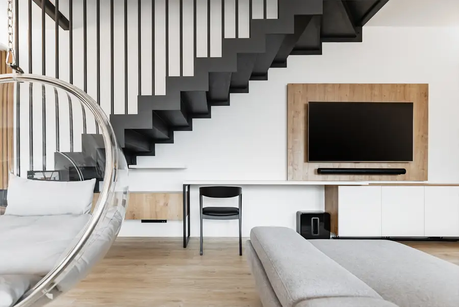 Minimalistický obývací prostor s černým schodištěm a dřevem